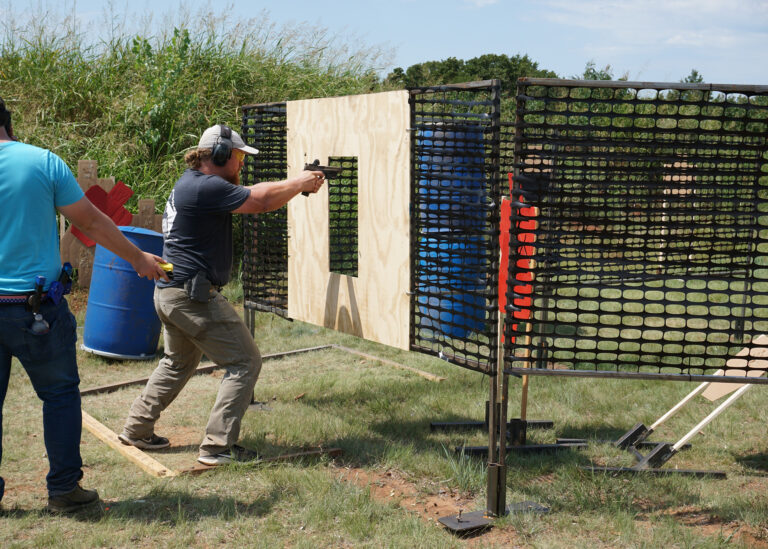 A competitor shoots from behind a barricade while a range officer stands alongside at the PCSL pistol match.