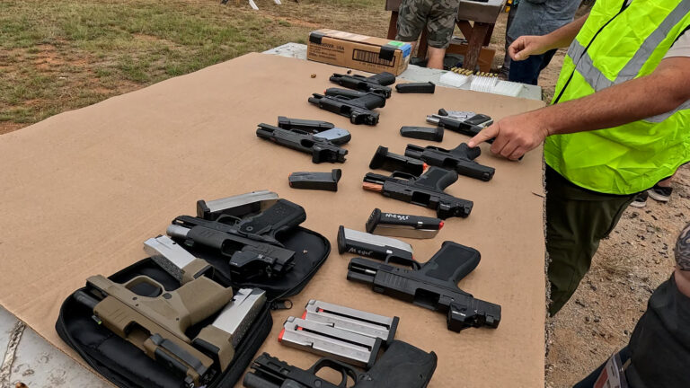 A club instructor points out one of the pistols available for participants to try, laid out on a shooting bench.