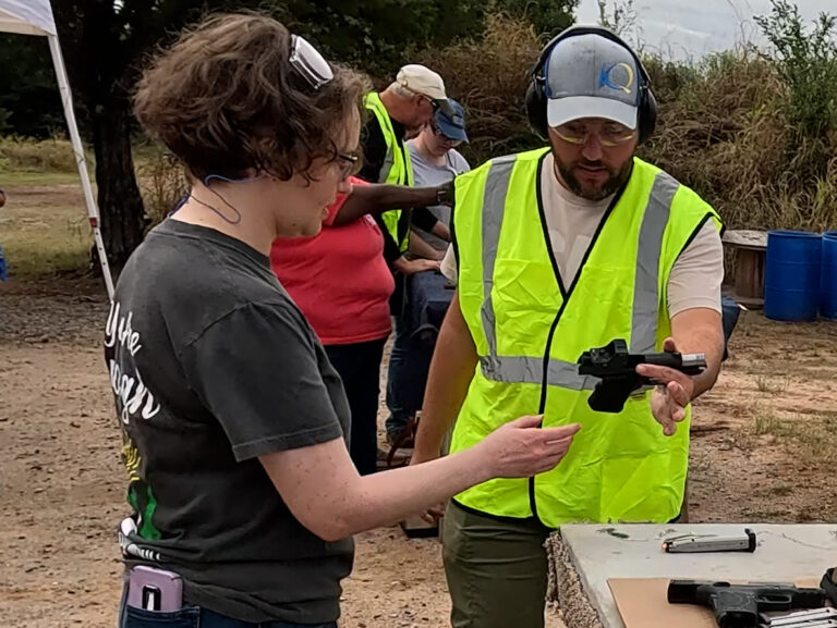 A club instructor hands a participant a pistol with the action open while explaining how to handle it.