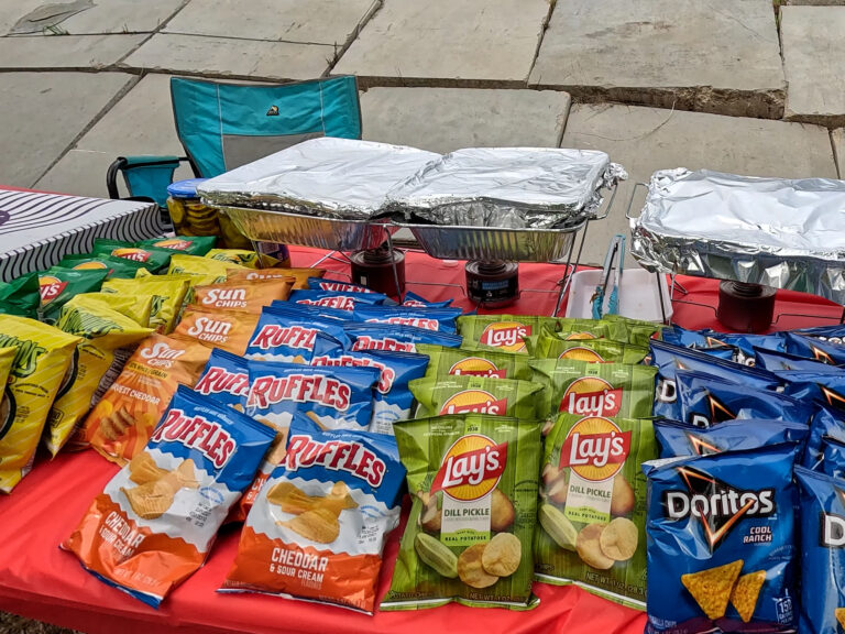 Lunch set out at the range, with warming trays, chips, and rolls on a covered table.