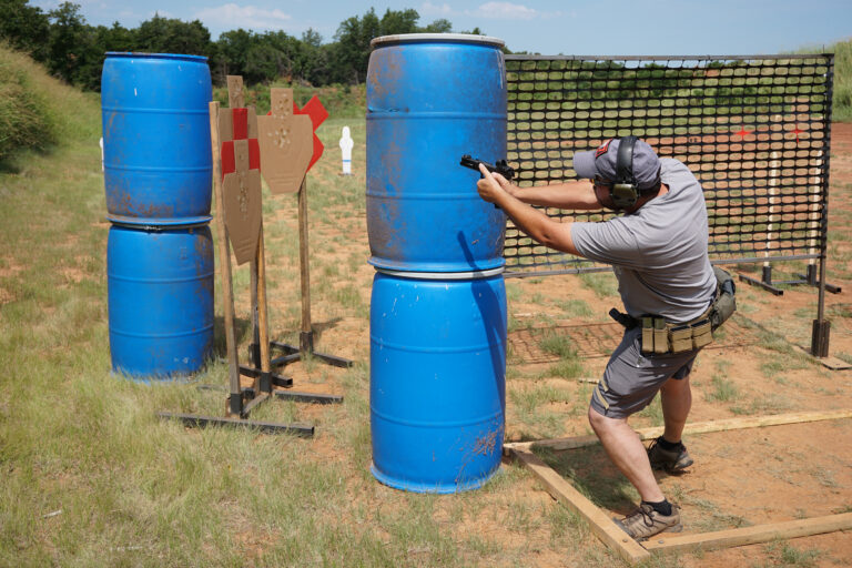 A competitor leans around a barrel barricade to engage targets at the PCSL pistol match.