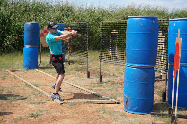 A competitor fires a pistol while moving past a barrel barricade during the PCSL pistol match.