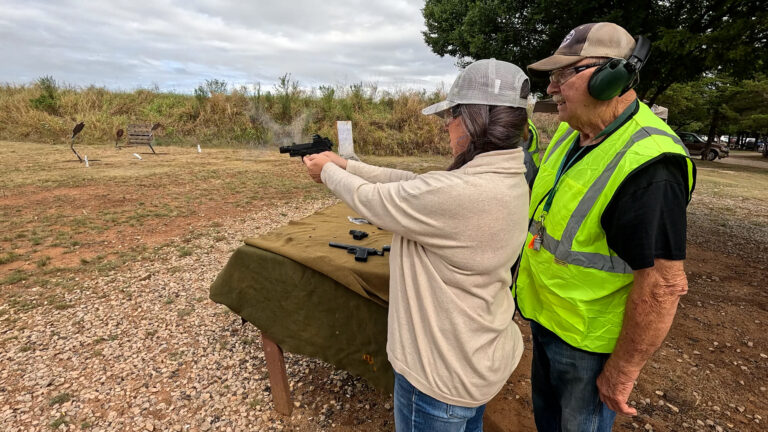 A club instructor watches closely as a participant fires at steel targets downrange.